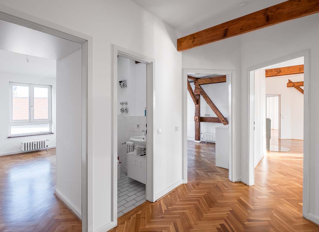 Vacant Home Insurance - Hardwood Floors and Exposed Wooden Beams of a Vacant Penthouse Apartment after a Renovation with Multiple Rooms and View of Bathroom