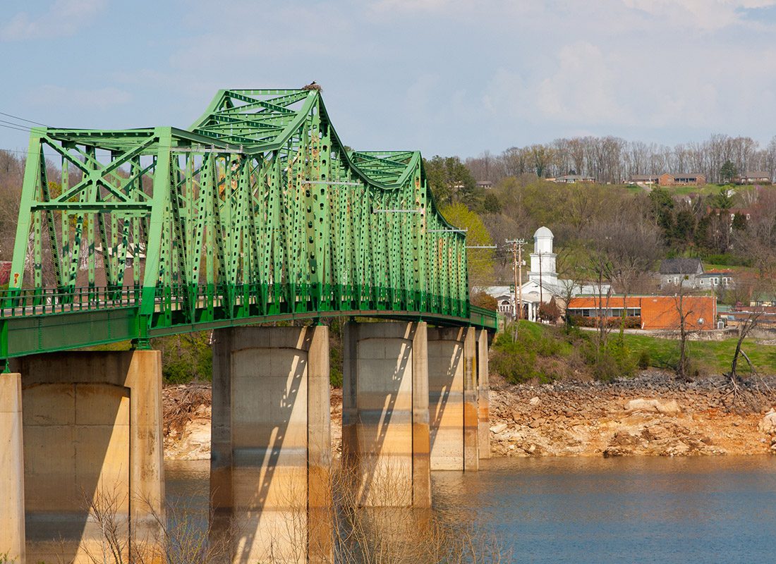 Dandridge, TN - Aerial View of a Green Bridge Crossing a River and Buildings in the Background on a Hill