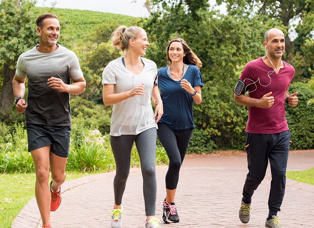 Employee Benefits - Group of Men and Women Jog Together Through a Park on a Brick Road on a Sunny Day