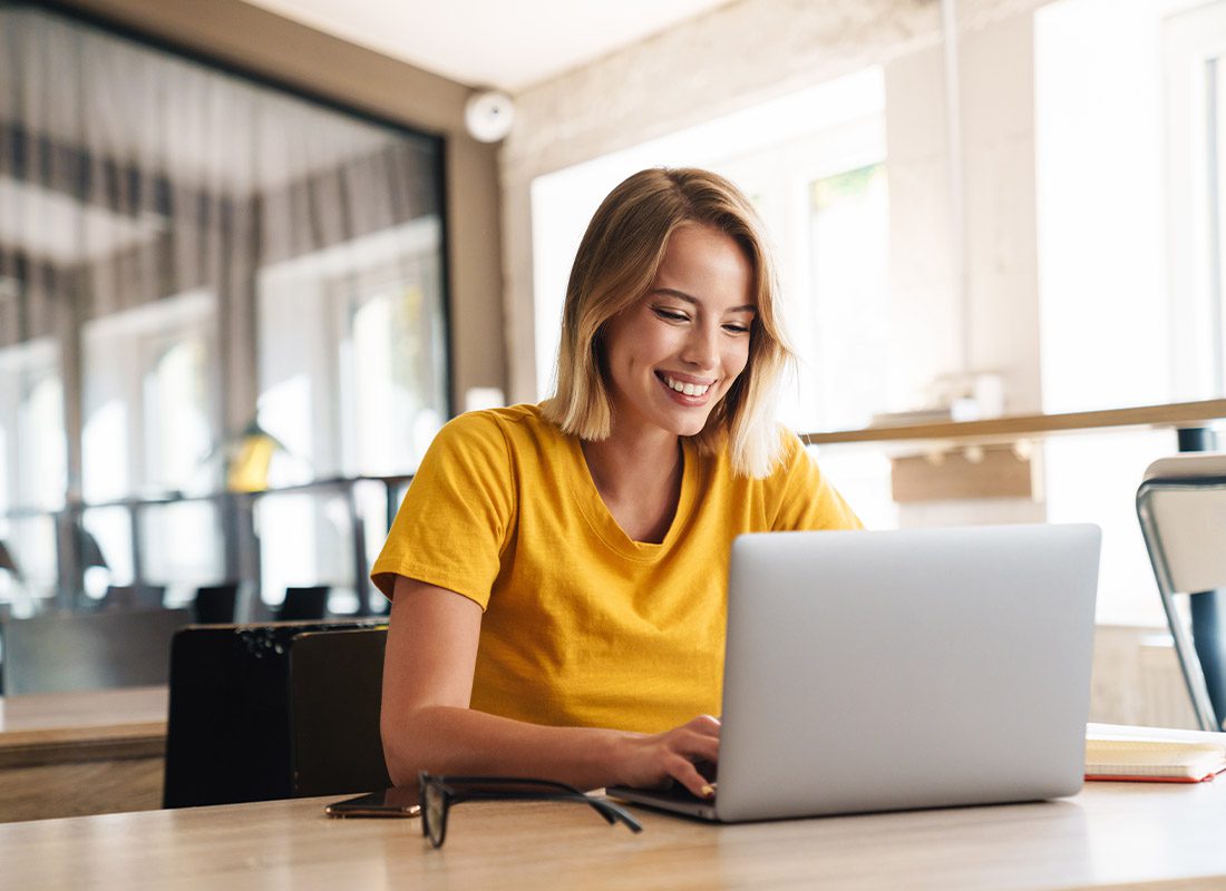 Blog - Smiling Woman Looking at Her Laptop in a Large Empty Modern Office